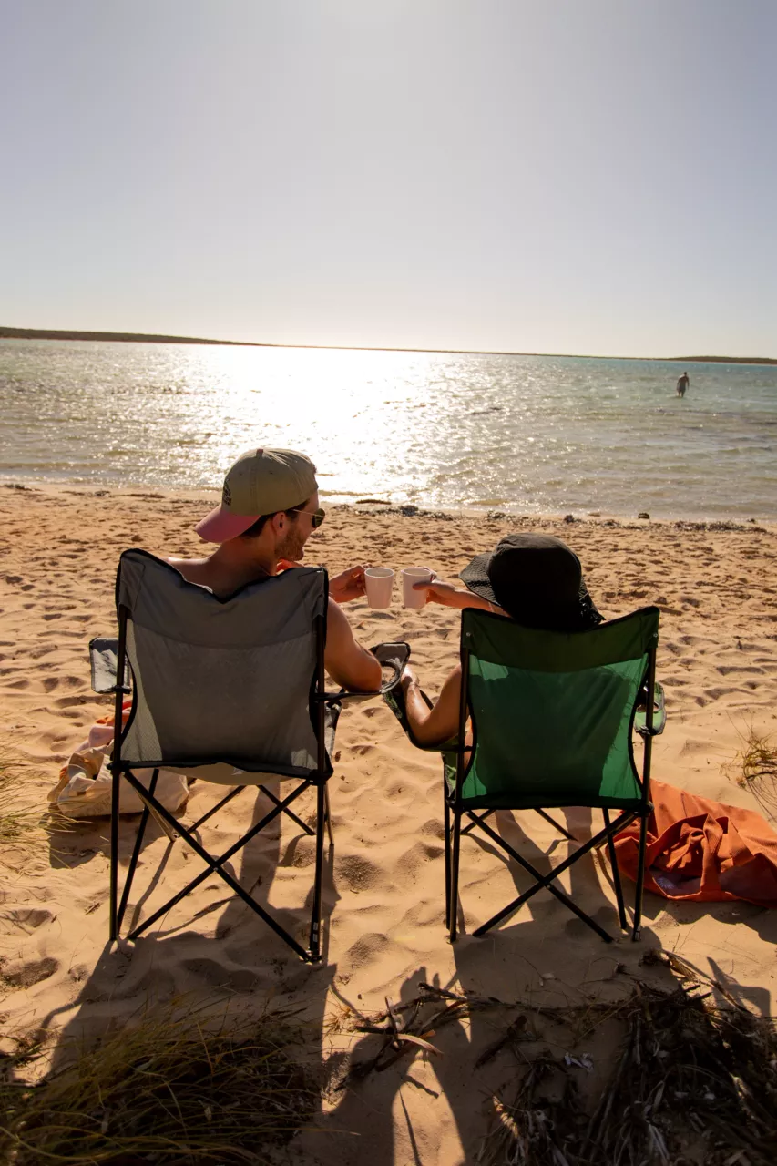 Two people sitting on camping chairs on the beach