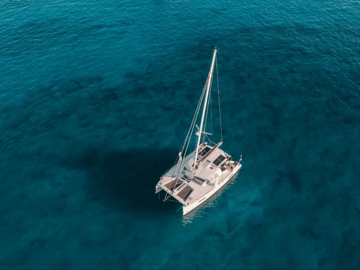 An aerial view of a catamaran on a turquoise sea.