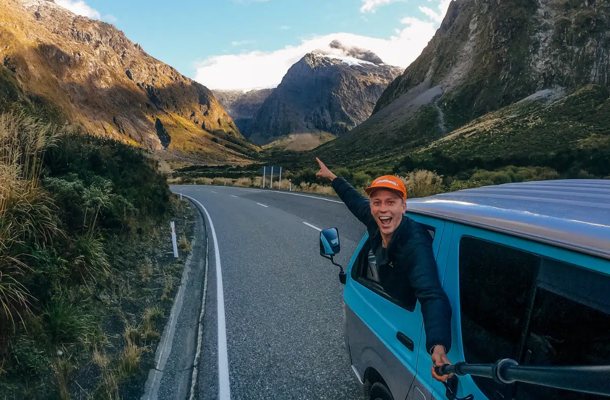 Buzzing RatPacker hanging out the window, pointing at a snow-capped mountain during an unforgettable NZ road trip adventure